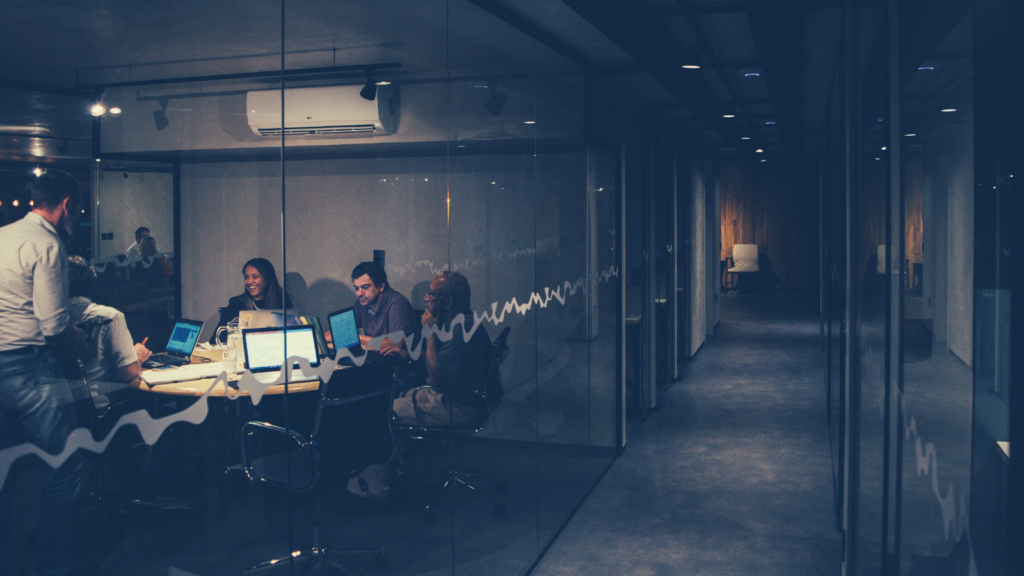 Startup employees sit around a table in a conference room at the end of a long hallway